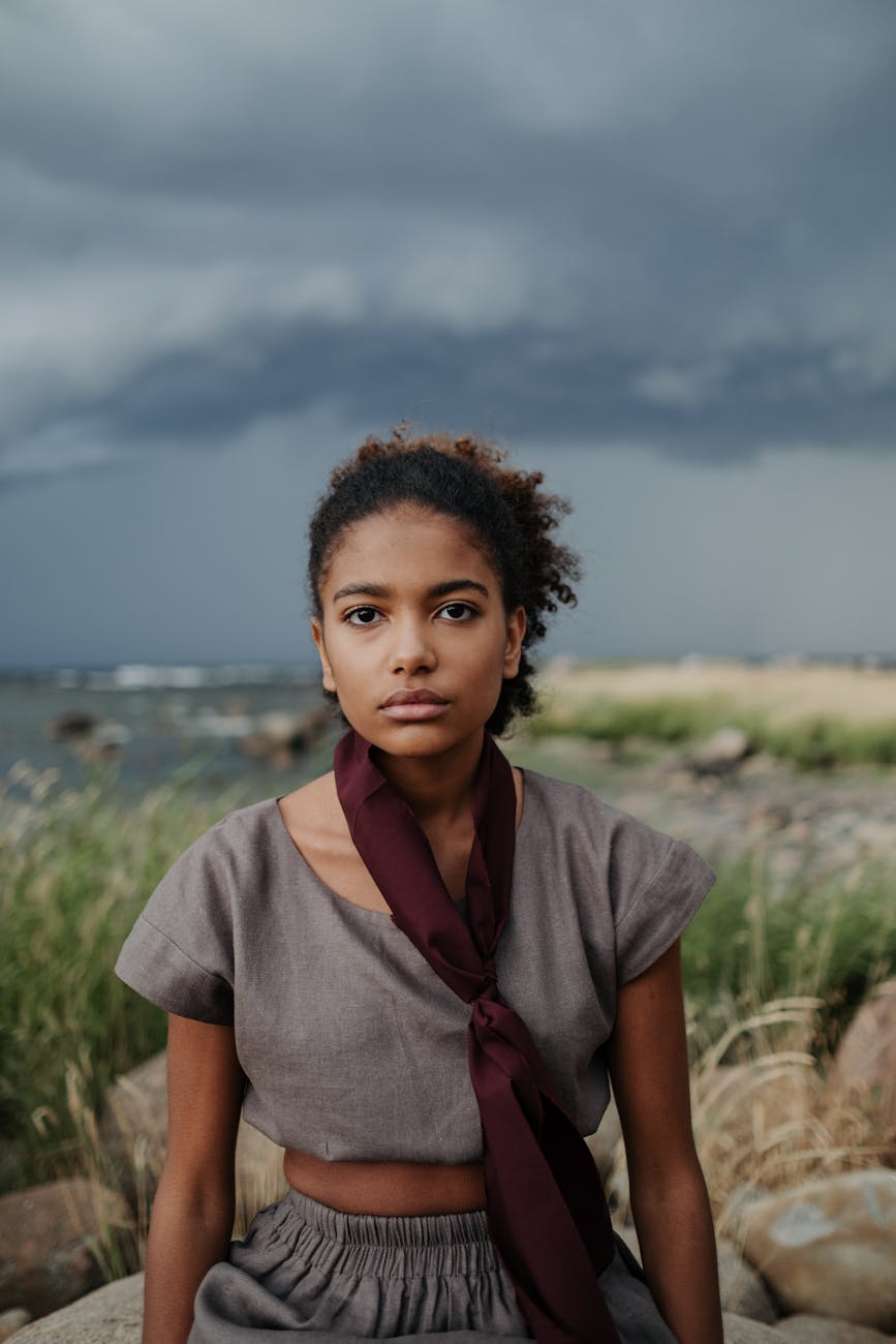 young woman in gray crop top with scarf sitting on a rock