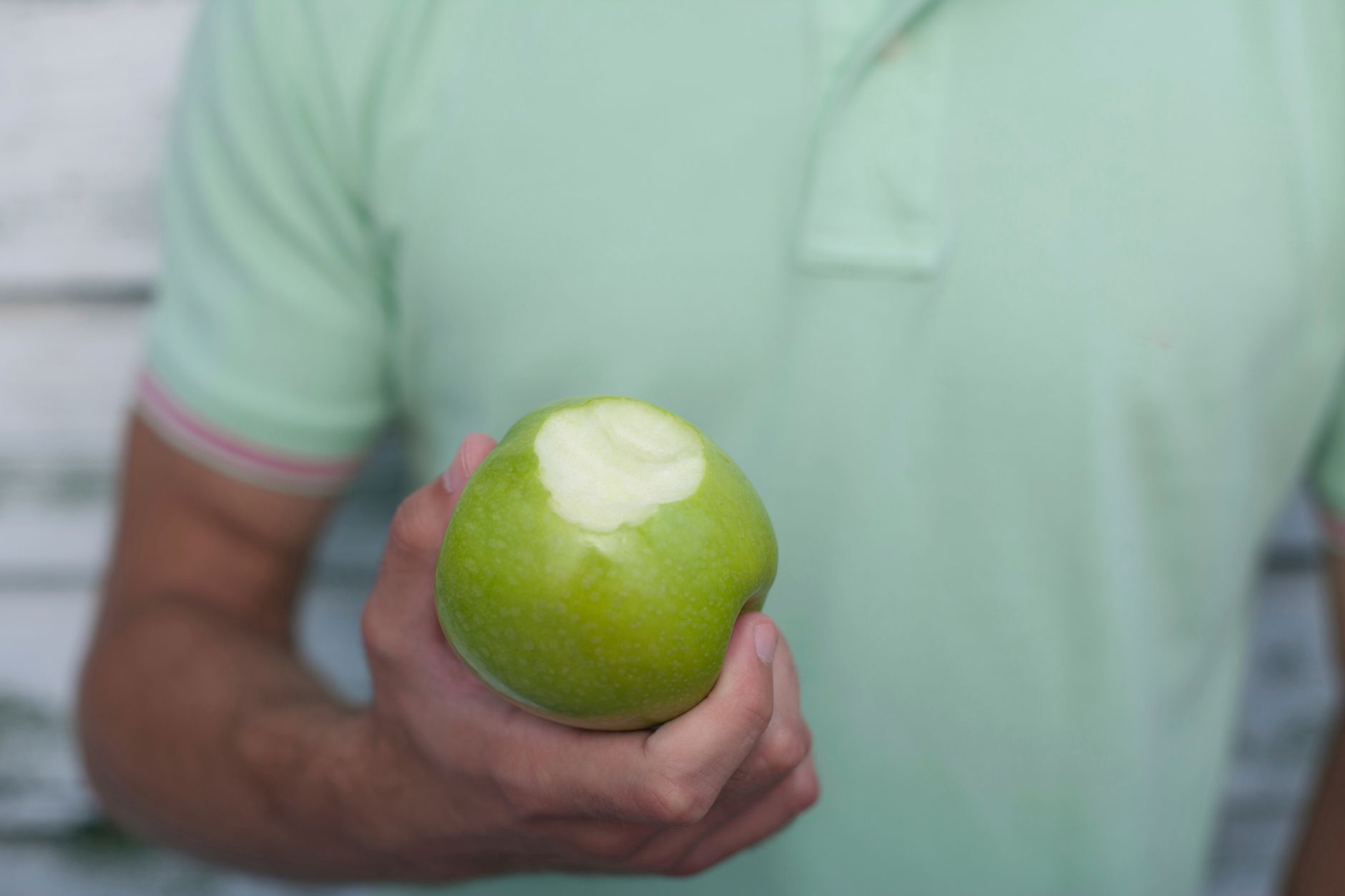 close up photo of a person holding green apple with bite